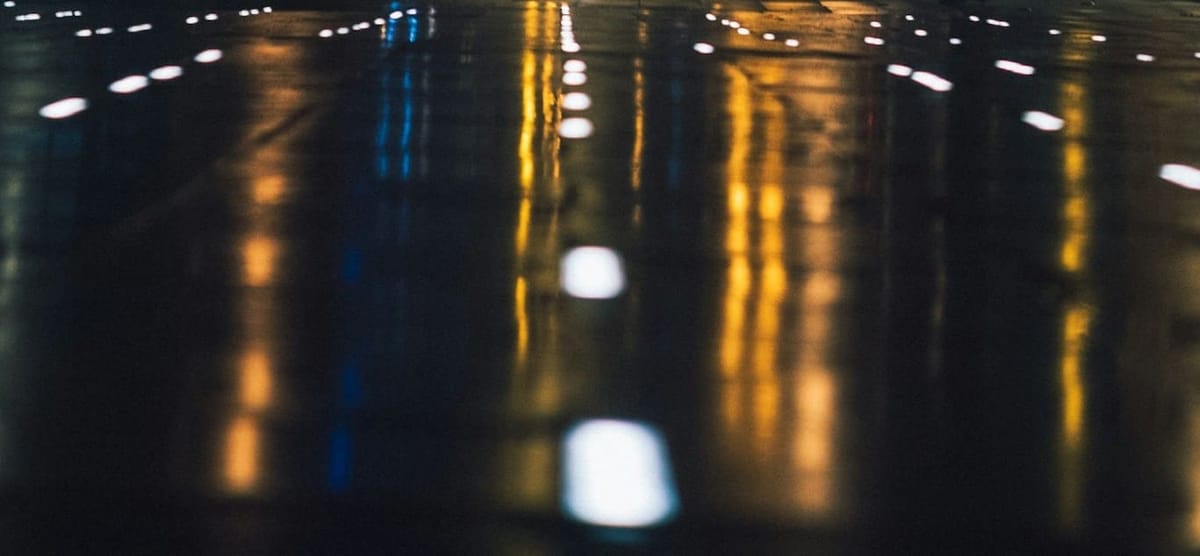 Blue and yellow streaked lights mirrored on a wide, wet, empty highway at night