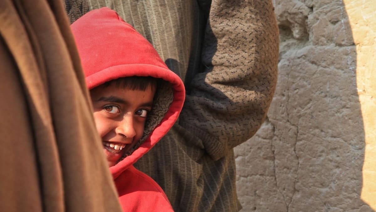 young child wearing a red hoodie is hiding between two adults and looking out gleefully