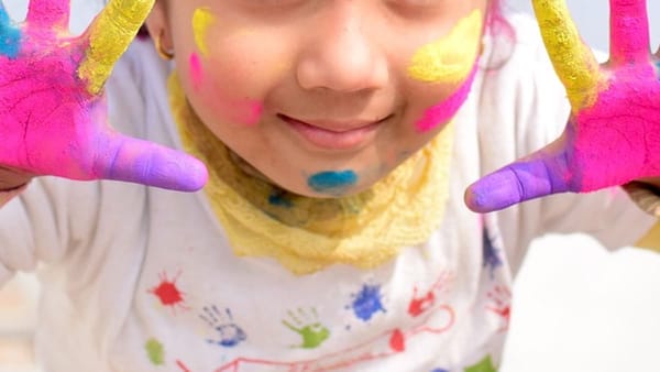 Kid with brightly painted hands, wearing a gold earring, smiling