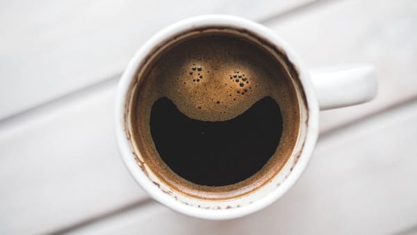 full coffee mug. the foam distribution makes the surface of the coffee seem as though it is grotesquely smiling.