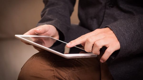 closeup of a person touching the screen of their tablet, balanced on their lap