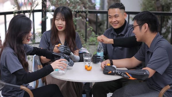 four friends, each with a prosthetic hand, sit at a table enjoying water and fruit