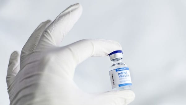 latex-gloved hand holds an mRNA vaccine vial