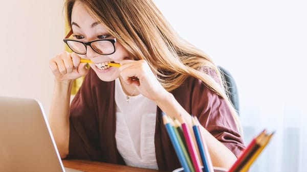 teenager gnaws pencil while staring at laptop